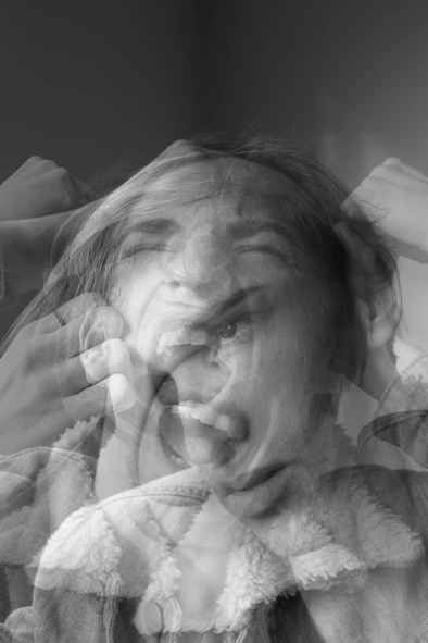 A black and white double exposure portrait of a person with hands near head