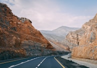 ashpalted road between brown mountain under blue sky