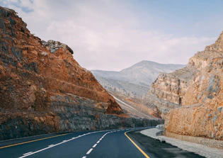 ashpalted road between brown mountain under blue sky
