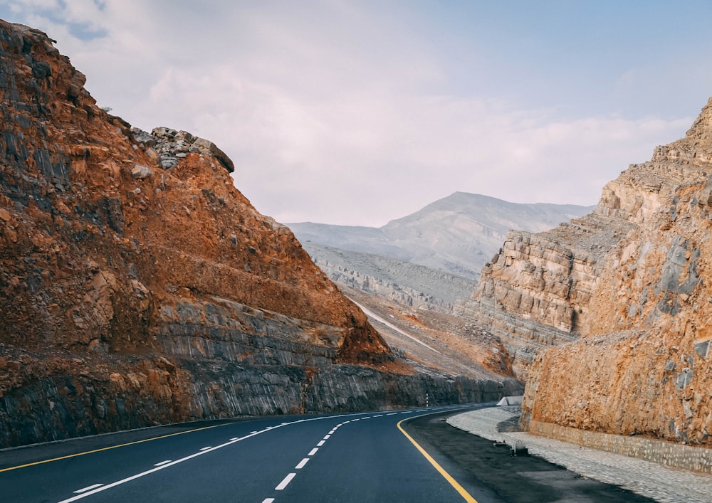 ashpalted road between brown mountain under blue sky