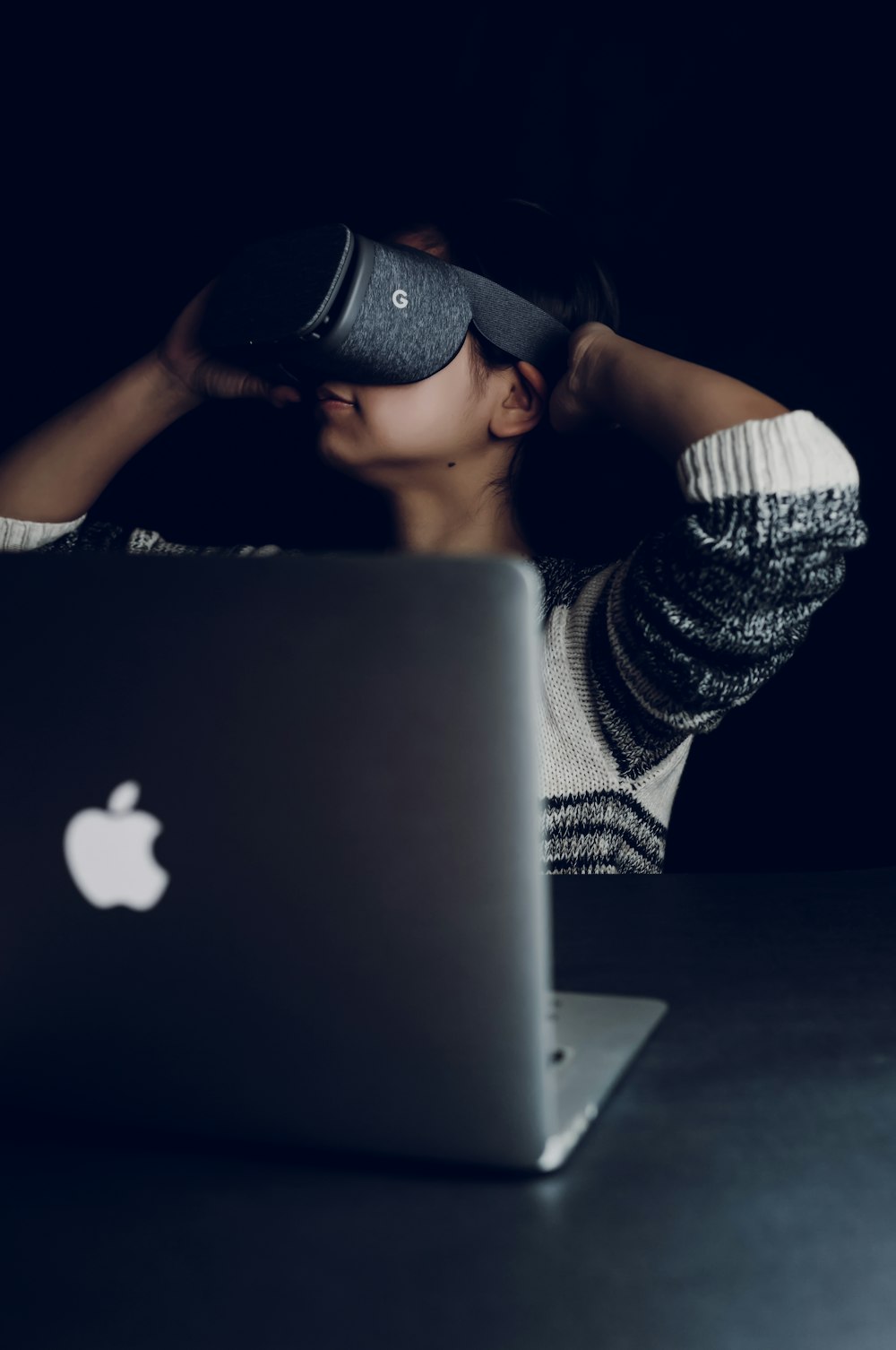 mulher usando fone de ouvido de realidade virtual preto virado para o MacBook