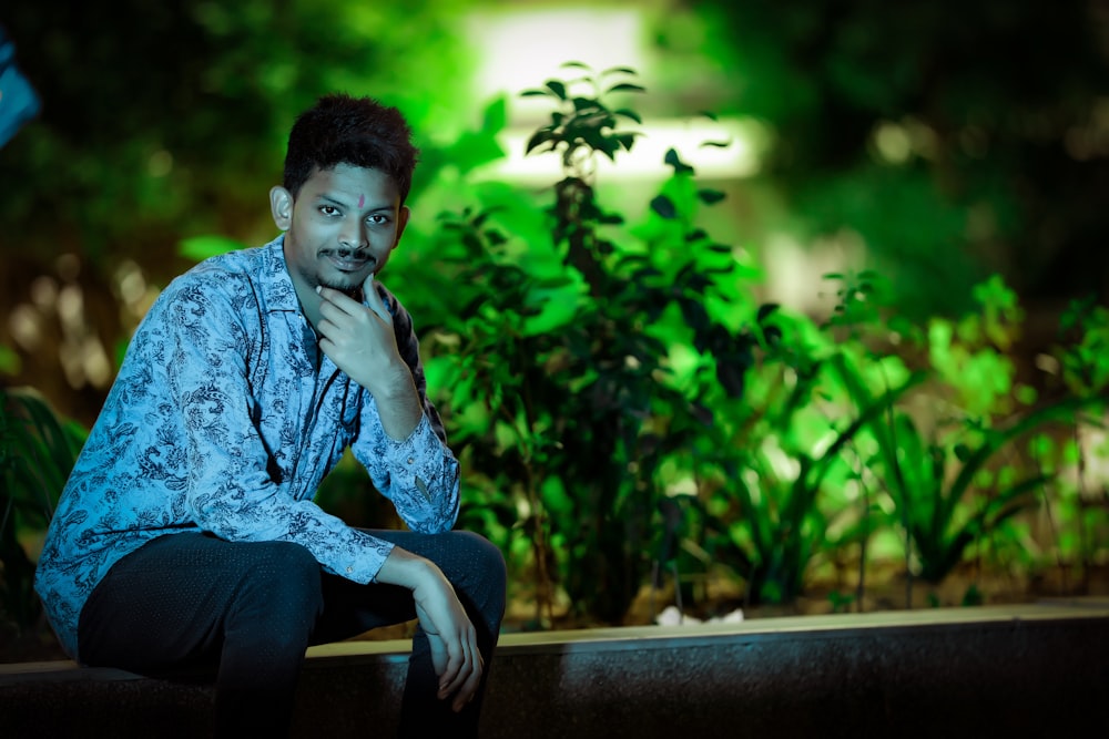 man wearing gray floral dress shirt and pants sitting on ledge near plants