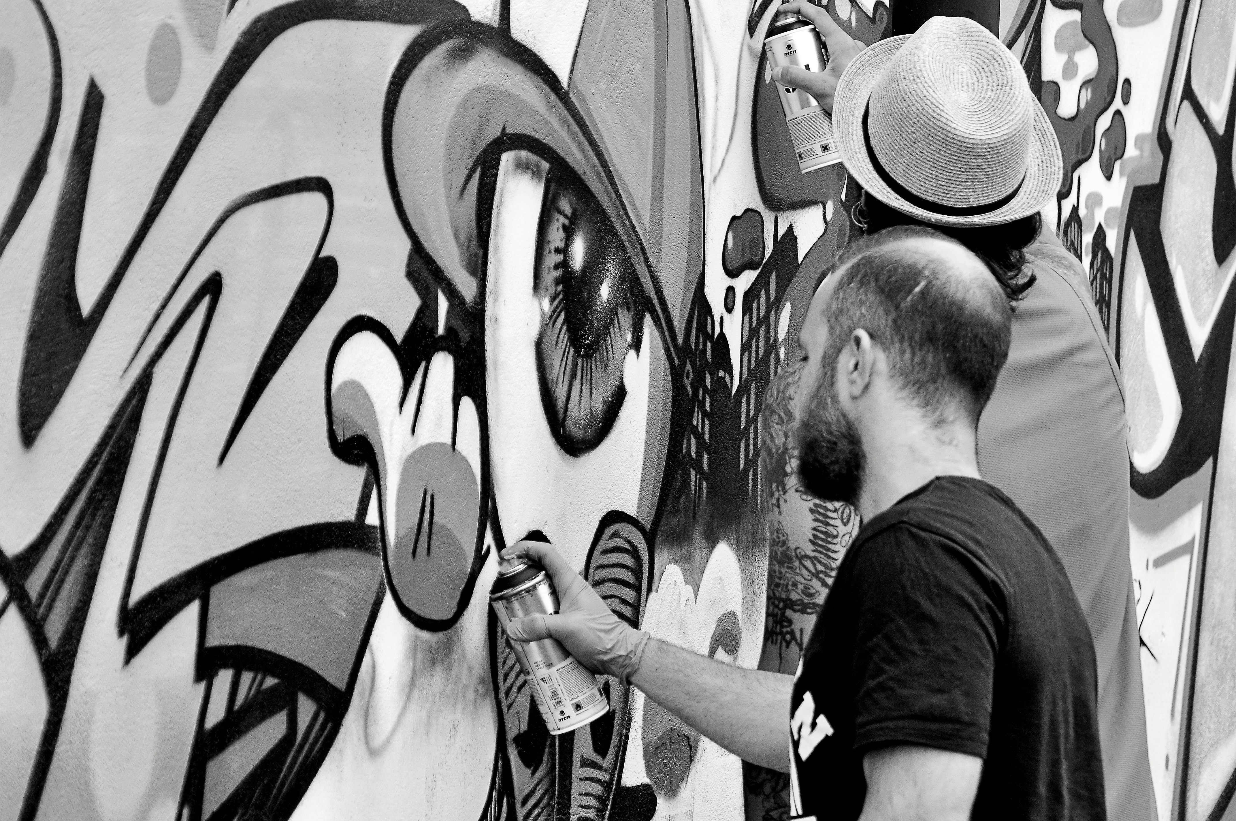 grayscale photography of two artists spraying graffiti wall
