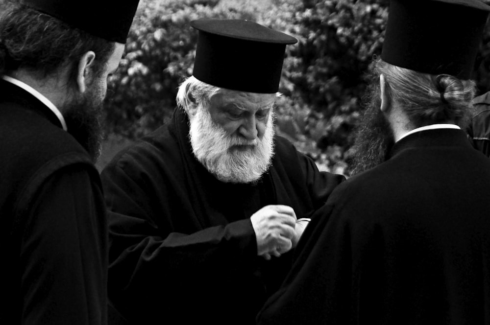 grayscale photography of three men wearing black robes and hats