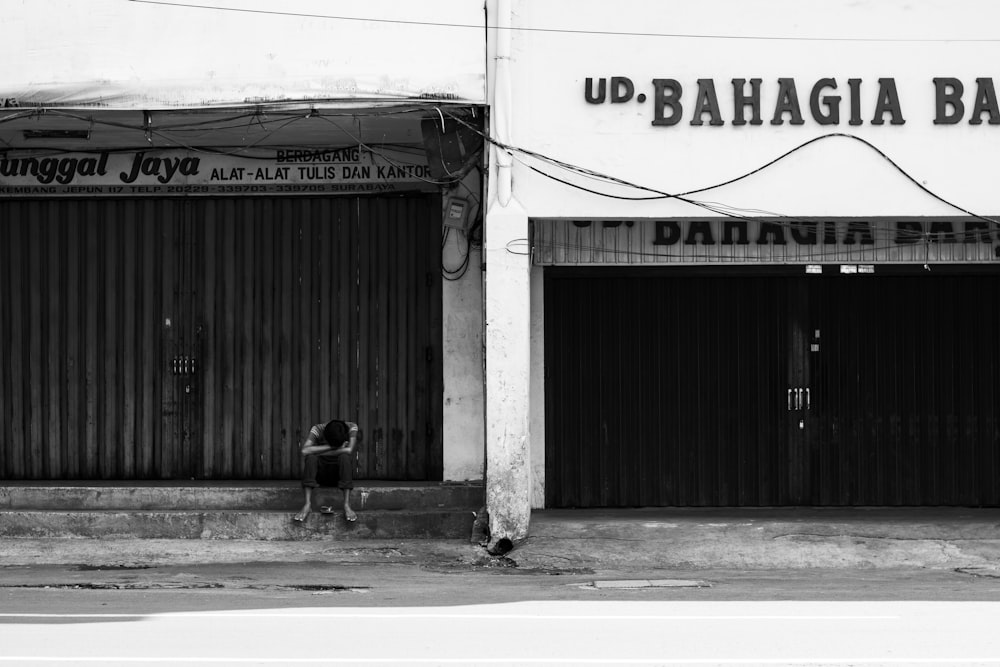 grayscale photo of person sitting building stair