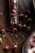 Dried rosebuds are scattered on a wooden surface, with some placed inside a small, transparent glass vial. The pink and purple hues of the rosebuds contrast starkly against the dark wood, creating a rustic and natural arrangement.