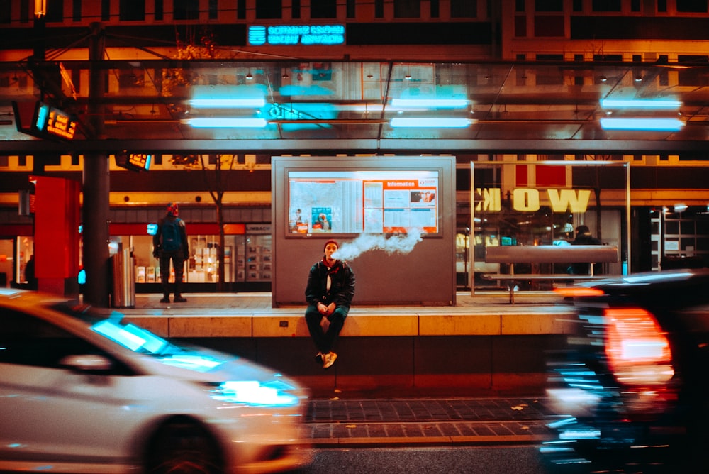 Zeitrafferfotografie eines Mannes, der nachts auf einem Felsvorsprung sitzt und raucht