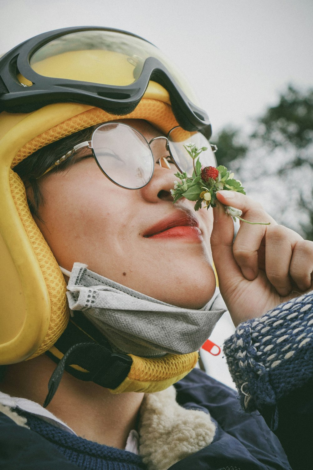 woman smells red flower while wearing helmet