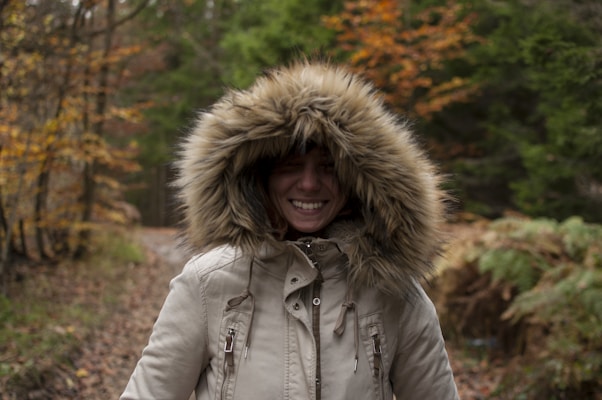 A stylish parka with fur-lined hood worn by a person walking through autumn leaves.