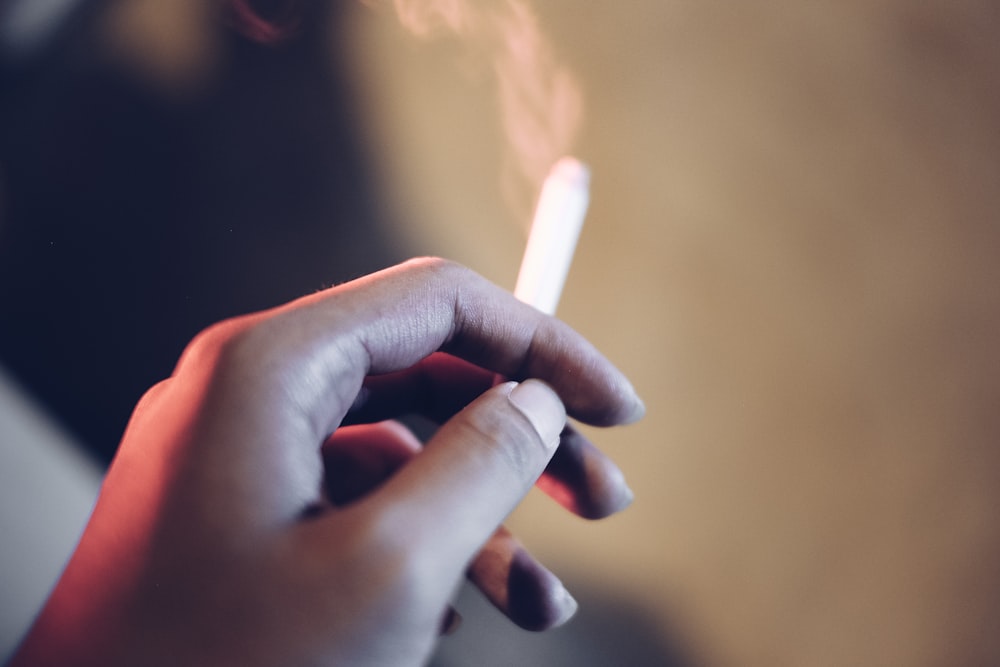 Fotografia a fuoco selettiva della persona che tiene la sigaretta accesa