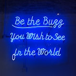 Bright blue neon letters against a dark background spell out an inspirational message in cursive font. The glow of the neon creates a striking contrast with the surroundings.
