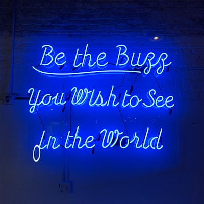 Bright blue neon letters against a dark background spell out an inspirational message in cursive font. The glow of the neon creates a striking contrast with the surroundings.