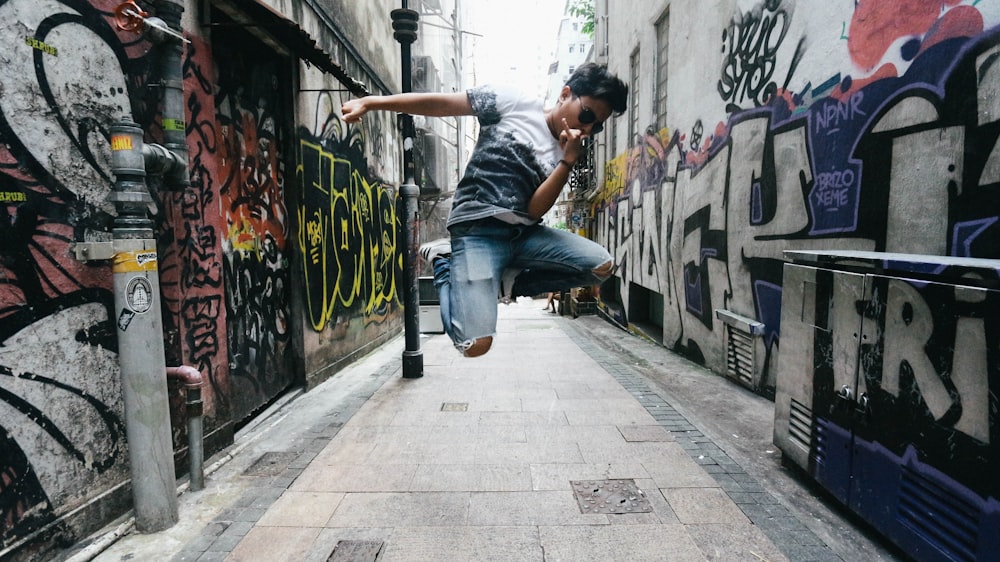 man wearing black t-shirt while jumping between concrete building