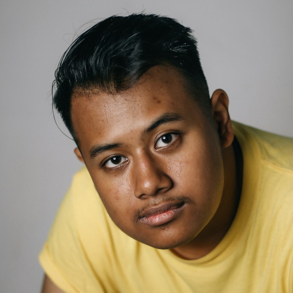 man wearing yellow crew-neck top near white wall