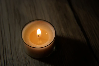 Close-up of a flickering handmade candle casting soft shadows on a wooden table.