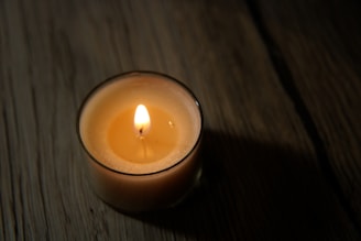 A cozy handmade candle glowing softly on a rustic wooden table.