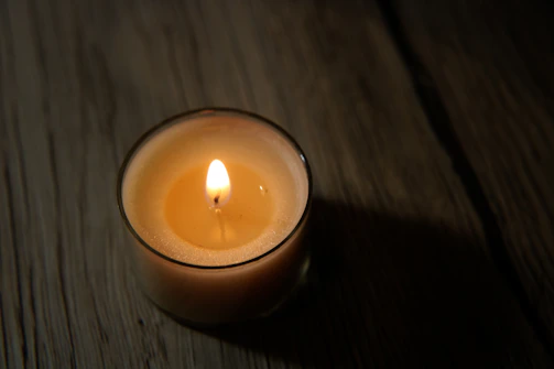 A softly glowing candle nestled in a rustic wooden holder, casting warm light on a cozy room corner.