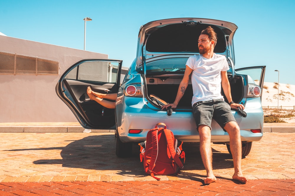 man sitting on car rear bumper