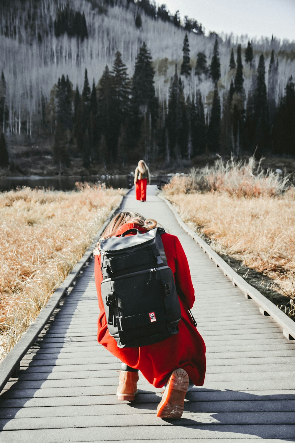 person wearing red cloth and black bag sitting on bridge in front of forest