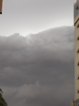 Dark gray storm clouds cover the sky, while a tall building with several windows is visible on the right side. The atmosphere appears overcast, suggesting an impending storm.