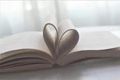 Hands holding a book with a heart-shaped bookmark, symbolizing care and inspiration.