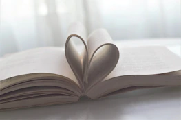 Hands holding a book with a heart-shaped bookmark, symbolizing care and inspiration.