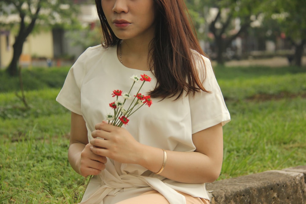 woman sitting on grey bench holding flower