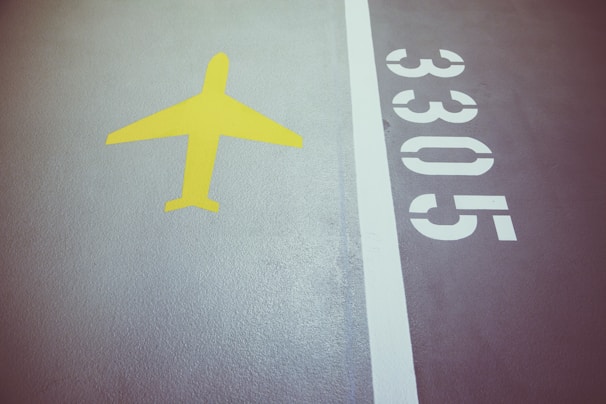 A section of pavement features a bright yellow airplane symbol to the left and the numbers 3305 in white on the right. A white line separates these elements on a textured surface.