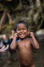 A cheerful toddler splashing in shallow water with a friendly instructor nearby.