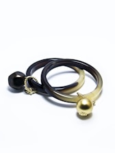Two intertwined bracelets with a smooth, dark finish. Each bracelet features a distinct decorative element: one with a large gold spherical charm, the other adorned with a unique darker bead. Both are connected by small gold chains, creating a sophisticated and elegant look.