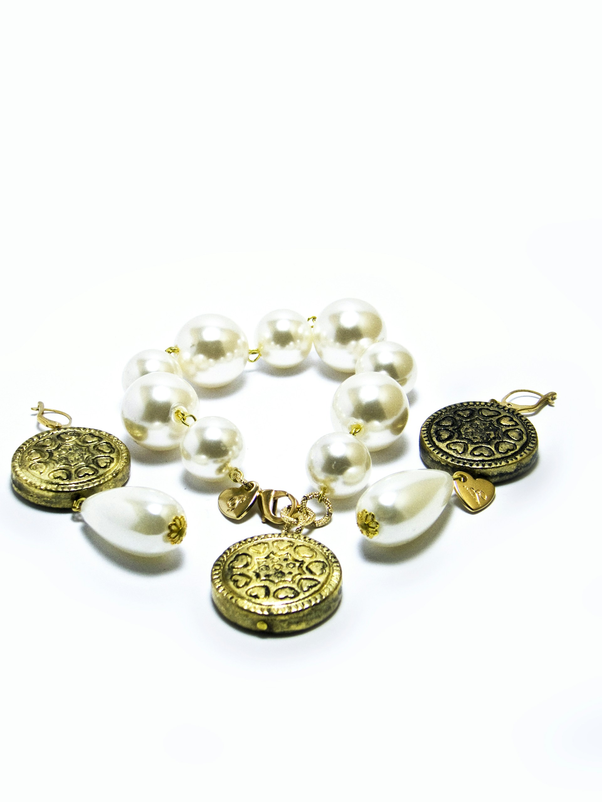 A bracelet composed of large, glossy white pearls and ornate gold coins, interspersed with teardrop-shaped white beads. The gold coins feature intricate engravings, adding a touch of elegance. The pearls and gold elements are linked together in a cohesive, stylish design.