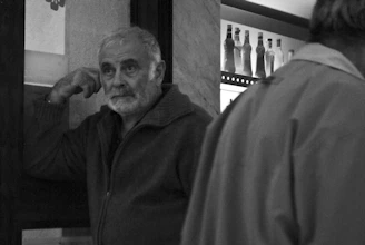 A candid shot of a man in a worn jacket leaning against the bar counter, lost in thought.
