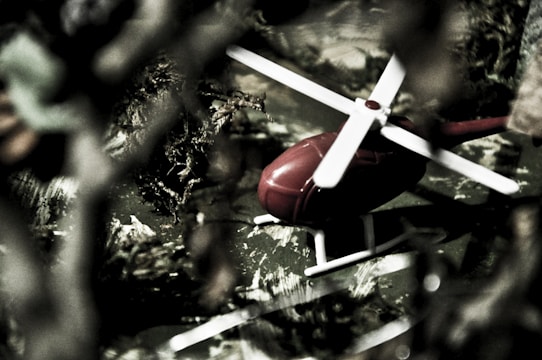 Close-up of a red toy helicopter flying outdoors against a clear blue sky.