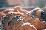Golden-brown croissants baked to perfection with a flaky crust and sprinkled with dark chocolate chips, glistening in natural sunlight streaming through a window.