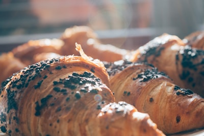 Golden-brown croissants baked to perfection with a flaky crust and sprinkled with dark chocolate chips, glistening in natural sunlight streaming through a window.