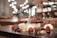 A close-up of a gourmet dessert plate featuring a mix of textures and colors. There are pieces of brownie, a scoop of berry sorbet, fresh raspberries, dollops of cream, and decorative sauces, all arranged artistically. The background is a softly lit, out-of-focus restaurant interior with warm tones and hanging lights creating a bokeh effect.