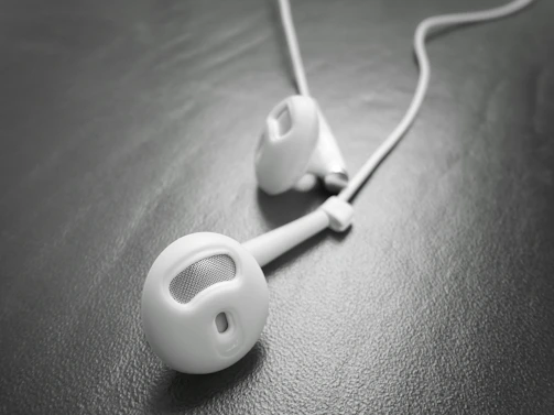 Close-up of sleek titanium in-ear monitor resting on a dark textured surface with warm gold accents.