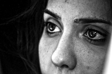 A close-up black and white photograph focusing intensely on a person's eyes, which are looking off into the distance. The image captures the fine details of the skin and hair, highlighting the texture and the deep, contemplative expression in the eyes.