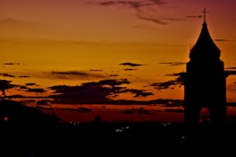 An old church steeple silhouetted against a dramatic sunset sky.