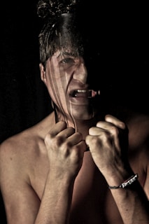 A distressed individual with hands clenched near their face, partially obscured by a dark vertical stripe across the image. The person appears to be expressing anguish or frustration, with a noticeable expression of strain.