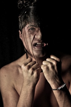 A distressed individual with hands clenched near their face, partially obscured by a dark vertical stripe across the image. The person appears to be expressing anguish or frustration, with a noticeable expression of strain.