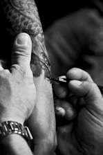 A close-up of an artist's hand applying intricate tattoo designs on a client's skin.