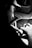 A person wearing a textured hat is focused on drawing or writing on a piece of paper. The setting is dimly lit, emphasizing the hand holding a pen and the concentration on the paper. A tablet or notebook is partially visible in the background.