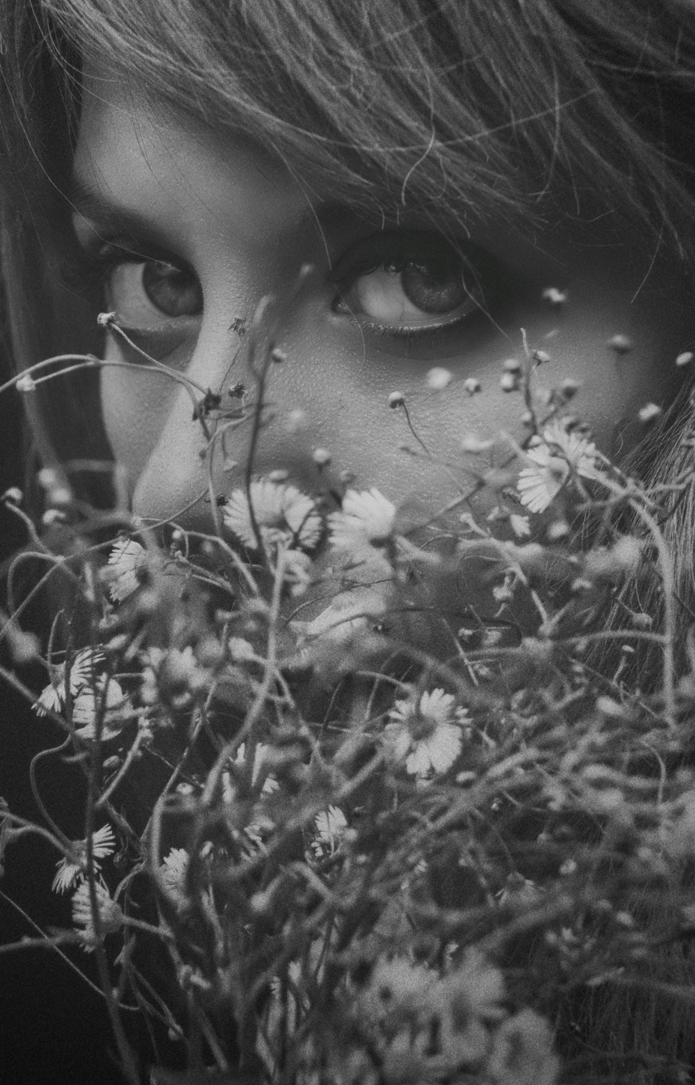 grayscale photo of woman behind flowers