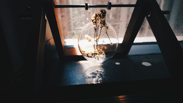 A sun catcher made from preserved wedding flowers catching soft sunlight against a black background.