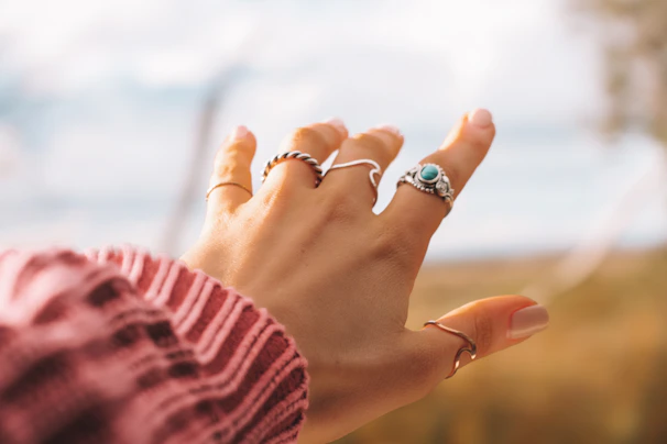 Soft-focus shot of a woman’s hand wearing layered rings against a dreamy pastel pink background.