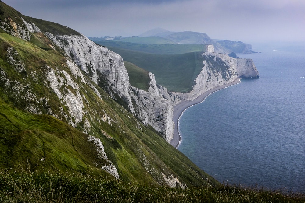 gray and green cliff beside body of water