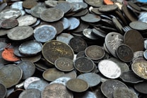 A large collection of assorted coins is spread out, showcasing various designs and denominations. The coins appear to be mostly old and have a variety of colors due to oxidation and wear. Some coins have distinct markings, such as numbers, figures, and symbols.