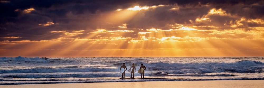 Tres hombres sosteniendo una tabla de surf frente a las olas del mar