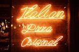 Neon sign with glowing orange letters reading 'Italian Pizza Original' against a dark background. The lighting creates a warm and inviting atmosphere, with visible reflections on the surface.
